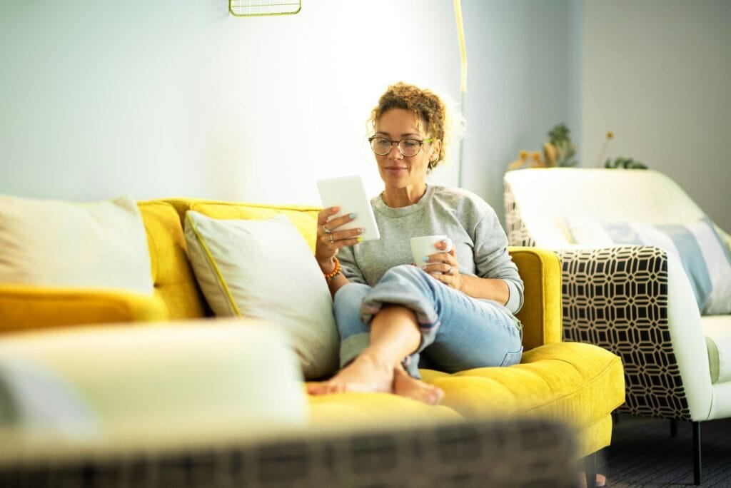 Modern middle age woman read an ebook on tablet sitting comfy on the sofa at home